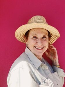 portrait of older woman wearing a hat smiling at the camera on red background